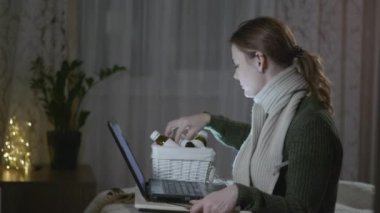 Viral hastalık ya da gribe yakalanan hasta kız, genç kadın termometreyle sıcaklık ölçer dizüstü bilgisayarla oturur ve internetten ilaç sipariş eder.