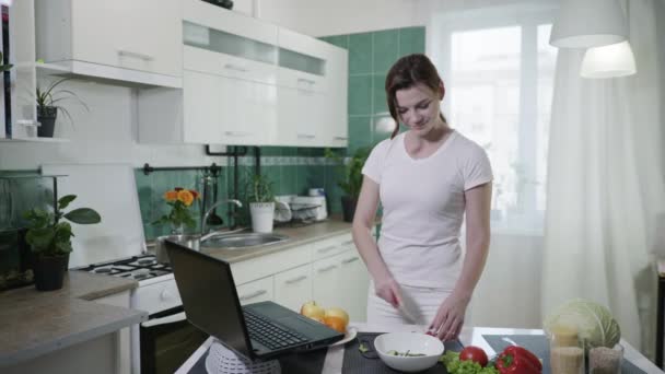 Gesunde ernährung, eine junge schöne frau auf diät bereitet frühstück aus nützlichen produkten nach video-rezept aus einem blog, schneidet frisches gemüse für vegetarischen salat — Stockvideo