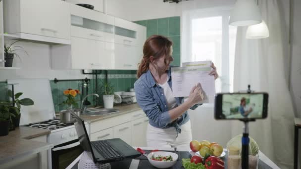 Women blog, young attractive housewife maintains blog and talks about diet plans and calories while standing in kitchen at table with fresh vegetables, people and social social networks — Stock Video