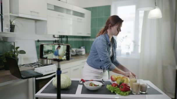 Home blog, moderne aantrekkelijke huisvrouw schrijft vlog video op mobiele telefoon praat over gezond voedsel en het verliezen van gewicht toont dieet plan terwijl staande aan tafel met verse groenten in de keuken — Stockvideo