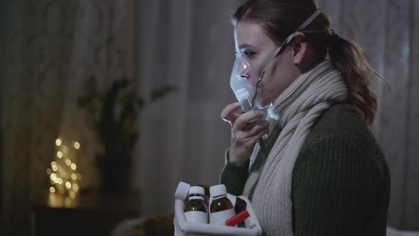Хвора жінка вдихає через інгаляторну маску в домашніх умовах, лікує запалення дихальних шляхів через туманність для запобігання астми та кашлю, сидячи на ліжку з ліками — стокове відео