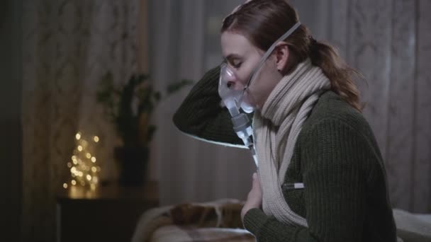 Хвороба, дівчина з поганим здоров'ям перевіряє температуру і дихає через інгаляторну маску, сидячи вдома на ліжку — стокове відео