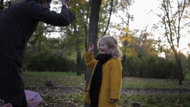 Jugar con un niño, mamá con una chica sonriente divertirse jugando tijeras de papel en una piedra para un paseo en el parque de otoño — Vídeo de stock
