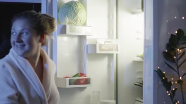 Dieta, uma dona de casa faminta feliz tira fast food da geladeira, jantares com bolo de donut doce e hambúrguer, danos à saúde — Vídeo de Stock