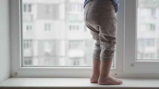 Az életet veszélyezteti, gyermeklábak sétálnak az ablakpárkányon, egy kisfiú veszélyben van az ablak közelében. — Stock videók