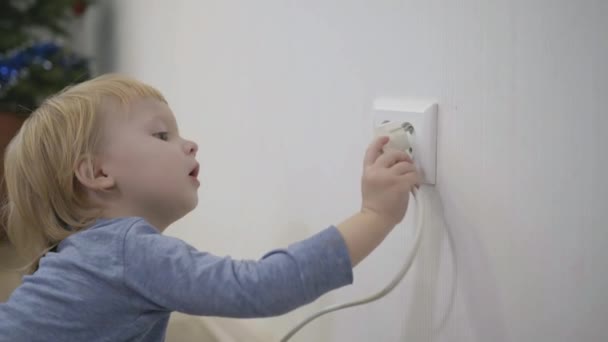 Criança tenta inserir uma tomada de energia em tomada elétrica close-up, um menino pequeno brincando perigosamente em casa — Vídeo de Stock