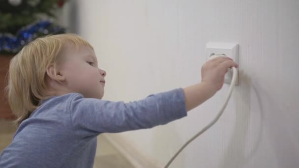 Criança em uma situação perigosa em casa, menino tenta inserir uma tomada de energia em tomada elétrica close-up — Vídeo de Stock