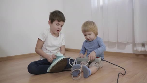 Niños curiosos juegan con objetos peligrosos, hermanos pequeños estudiando la plancha eléctrica y el enchufe sentado en el suelo de la habitación — Vídeo de stock