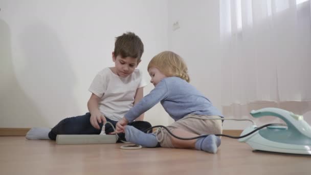 I bambini giocano pericolosamente con il cavo di prolunga elettrico, i bambini collegano la spina metallica dal ferro alla presa sul pavimento in camera — Video Stock