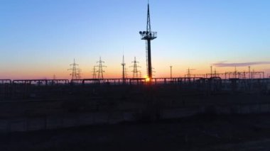 Güzel gökyüzü ve turuncu gün batımının altında yüksek voltajlı elektrik kuleleri ve elektrik hatlarının drone görüntüsü