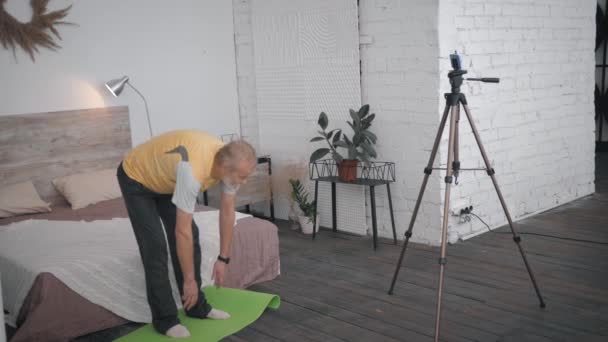 Peppy Influencers oudere man blogger schrijft nuttige oefeningen voor zijn volgers van sociale netwerken naar smartphone in de ruimte met een creatief interieur — Stockvideo
