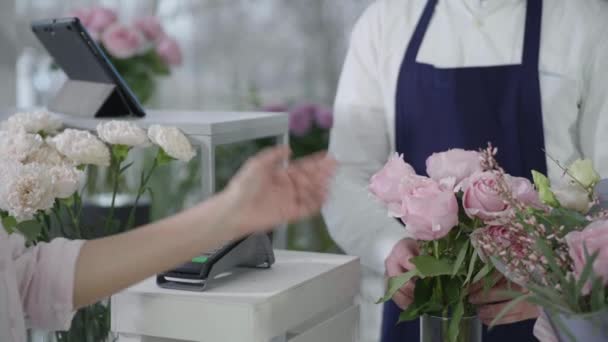 女买主在一家现代花店里买漂亮的花束，用智能手机在终端上进行无接触式支付，生意成功 — 图库视频影像