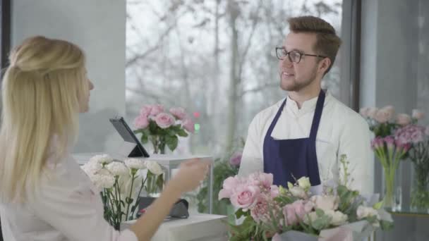 Successful small enterprises, young happy entrepreneur rejoices in good sales in flower shop, works at cash register selling beautiful bouquets of flowers, payment — 비디오