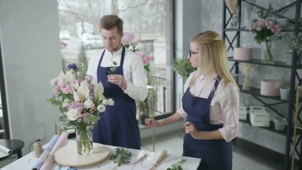 Ομαδική εργασία, εκπρόσωπος του επαγγέλματος του φύλου αρσενικό ανθοπωλείο συλλέγει μπουκέτο από όμορφα λουλούδια αναμειγνύεται με τη γυναίκα συνάδελφό της στη σύγχρονη μπουτίκ λουλουδιών — Αρχείο Βίντεο