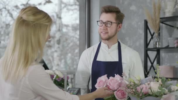 Jonge zakenman, mannelijke startup kleine ondernemer van moderne bloemenwinkel verkoopt boeket bloemen aan gerl, vrouw betaalt voor de aankoop door contactloze betaling met behulp van smartphone — Stockvideo