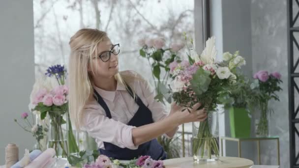 Молодая счастливая женщина флорист делает современный букет для продажи в цветочном магазине, женщина-предприниматель, представитель гендерного равенства заботится о малом бизнесе — стоковое видео