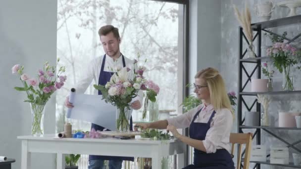 Květinářství, mladí profesionálové květinářství chlapec a dívka vytvořit krásné moderní kytice kvetoucích květin ve váze, týmová práce — Stock video