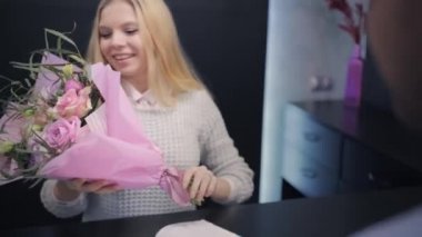 Çekici, mutlu, sarışın kız güzel bir buket çiçek alır, müşteriyle ilgilenen çiçekçi, internetten çiçek siparişi verir.