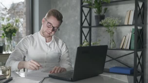 Technologies modernes dans les affaires, portrait de jeune homme attrayant dans des lunettes pour la vision de travail à des idées d'écriture d'ordinateur portable dans le cahier, enseignement à distance — Video
