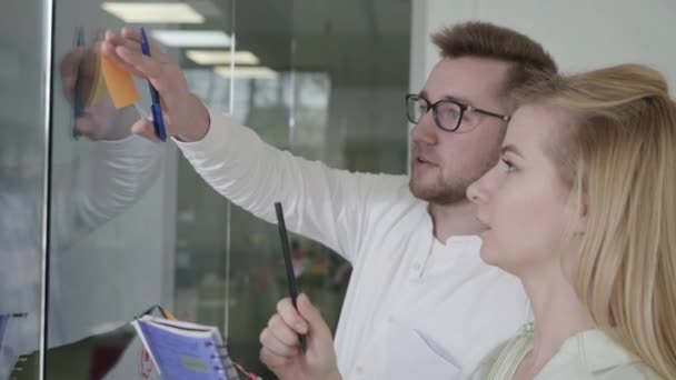 Equipe de funcionários fica no conselho de planejamento no escritório e pendura adesivos adesivos distribuindo plano de trabalho, reunião — Vídeo de Stock