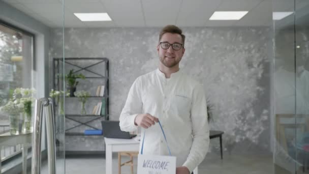 Malý obchodní úspěch, atraktivní mladý podnikatel se raduje z otevření obchodu a stojí s cedulí otevřenou v rukou — Stock video