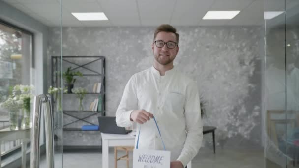 Sucesso de pequenos negócios, atraente jovem empreendedor se alegra com a abertura da loja e fica com um sinal aberto em suas mãos — Vídeo de Stock