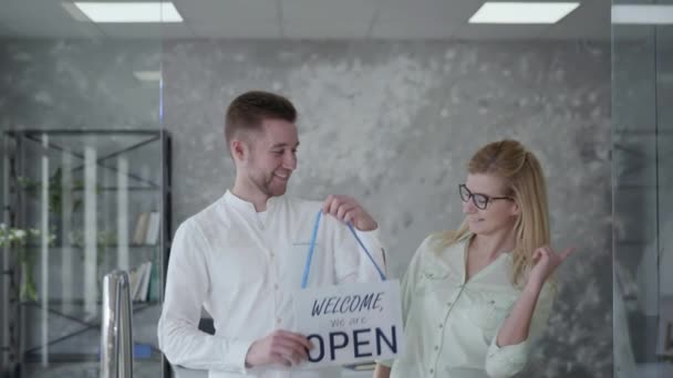 Éxito de la puesta en marcha, jóvenes socios de negocios felices hombre y mujer con un signo abierto, los colegas se alegran por la apertura de una tienda, pequeña empresa — Vídeos de Stock