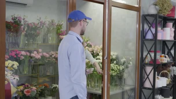 Klein bedrijf, een jong meisje werkt in een bloemenwinkel geeft een prachtig boeket bloemen aan een man van een bezorgservice, een concept van succes — Stockvideo