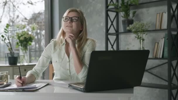 Happy smiling woman working at computer in to office with fresh flowers, rejoicing for success young business woman used laptop for online service, checks orders and writes data in notebook, business — Stock Video