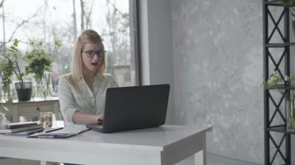 Sikeres startup, fiatal női vállalkozó szemüveggel a látás élvezi az üzleti siker, miközben ül asztalnál laptop boldog nő táncol a munka, virágos belső — Stock videók