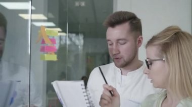 İş adamları erkek ve kadın cam beyaz tahta üzerine yapışkan notlar kullanıyor. Beyin fırtınası yapan takım lideri kadın iş arkadaşlarıyla çalışıyor. Ofis toplantısında sorun çözme stratejisi gösteriyor.