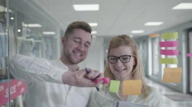 Ofis, dost canlısı takım adamı ve kadın yapışkan çıkartmalar ve beyin fırtınalarıyla cam panoların yanında oyun oynuyorlar.