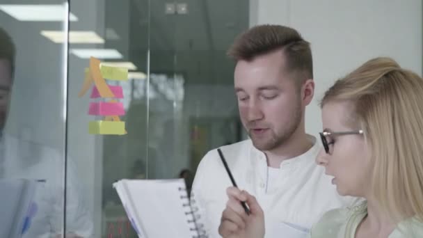 Business people man and woman using sticky notes on glass whiteboard brainstorming team leader woman working with colleagues male showing problem solving strategy in office meeting — Stock Video