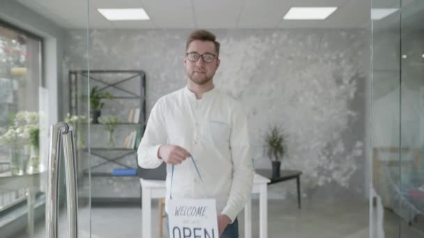 Pequeños negocios, retrato de un joven atractivo sosteniendo un cartel abiertamente en sus manos, un exitoso hombre de negocios se regocija por la apertura de una tienda — Vídeos de Stock