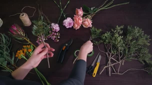 Floristic business concept, professional florist makes modern bouquet of beautiful fresh flowers on dark background, hands closeup — ストック動画