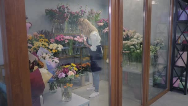 Young female florist works in greenhouse, checks flowering for making bouquet for delivery, flower shop — Stockvideo