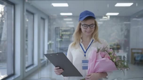 Young smiling girl with glasses and cap works in delivery service, female employee delivers bouquet of flowers to address taking care of client, small business — ストック動画