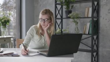 happy calm woman holds hands behind head feeling relieved relaxes and sits at home office with beautiful fresh flowers interior desk with laptop, female student enjoys successfully completed work