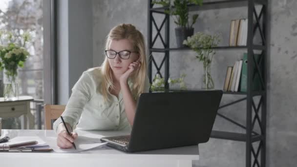 Happy calm woman holds hands behind head feeling relieved relaxes and sits at home office with beautiful fresh flowers interior desk with laptop, female student enjoys successfully completed work — Stok video