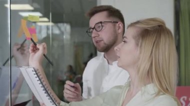 friendly colleagues man and woman talk about planning work on notes, happy employees write creative ideas on sticky stickers