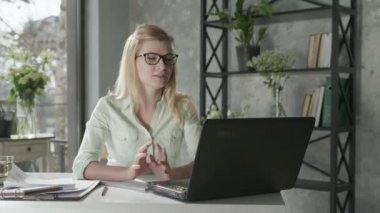 female entrepreneur discussion video calls with business partner sitting at table with laptop in office next to beautiful bouquet of flowers, communicating online concept