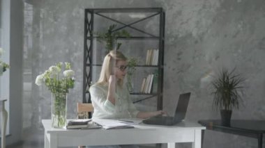 girl works at a computer, happy business woman in modern office with floral interior at laptop checks online bookkeeping background of fresh flowers, small business