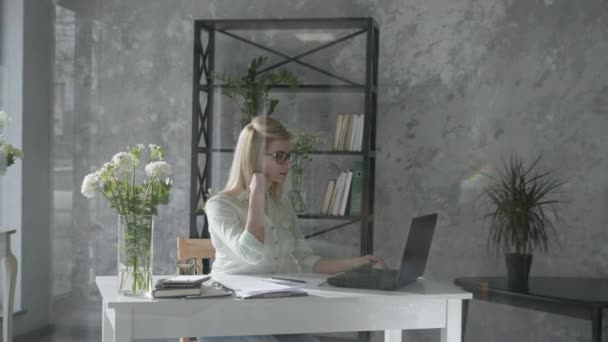 Girl works at a computer, happy business woman in modern office with floral interior at laptop checks online bookkeeping background of fresh flowers, small business — Wideo stockowe