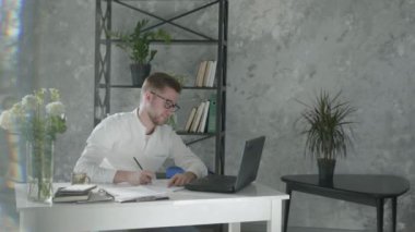 modern computer technologies in online business, successful entrepreneur man works with laptop and takes notes in notebook to planning business ideas in an office with modern plants interior on
