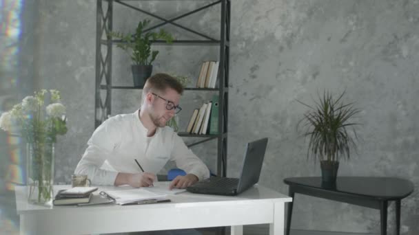 Modern computer technologies in online business, successful entrepreneur man works with laptop and takes notes in notebook to planning business ideas in an office with modern plants interior on — Stockvideo