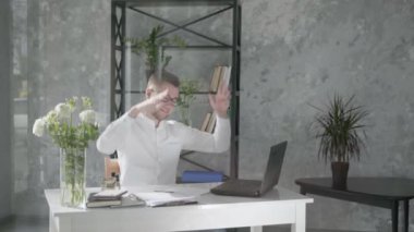 happy businessman small business owner works in an office with a modern floral interior on background of fresh bouquets of flowers at computer, satisfied with successful work throws hands behind head