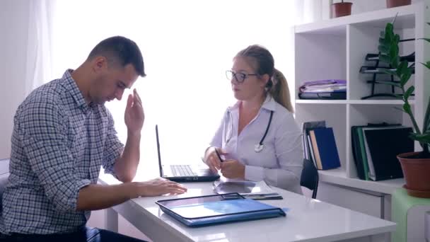 Läkare med röntgen säger dåliga nyheter upprörd man patient på läkarmottagningen — Stockvideo