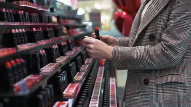 Girl chooses makeup cosmetics, tests lipstick while shopping at cosmetics store, close-up — Wideo stockowe