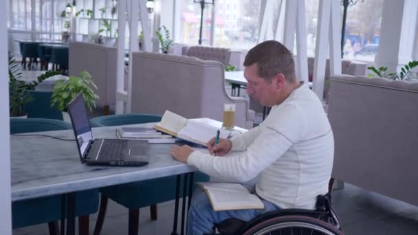 Distance education of invalid, successful sick student male on wheelchair working with laptop to learn from online lessons and making notes in notebook — Stockvideo