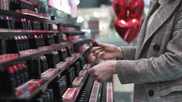 Maquillaje, comprador femenino en una tienda de cosméticos prueba lápiz labial rojo en la mano durante la venta de temporada, primer plano — Vídeo de stock